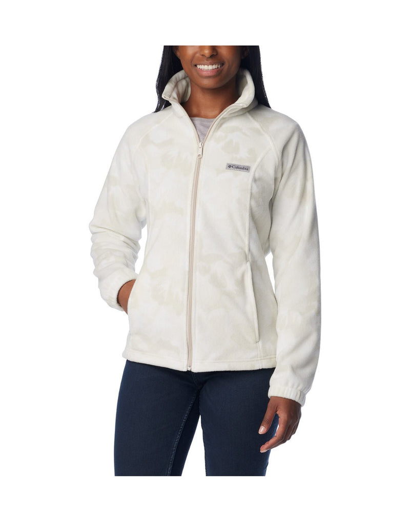 Woman wearing dark blue jeans and Columbia Women's Benton Springs™ Printed Full Zip Fleece Jacket in dark stone peonies, white with light beige floral pattern, front view, zipped up with one hand in pocket