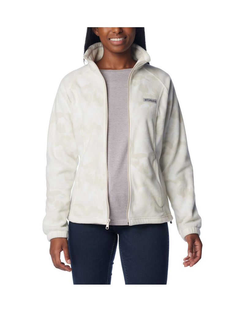 Woman wearing dark blue jeans and Columbia Women's Benton Springs™ Printed Full Zip Fleece Jacket in dark stone peonies, white with light beige floral pattern, front view, unzipped, with grey t-shirt beneath