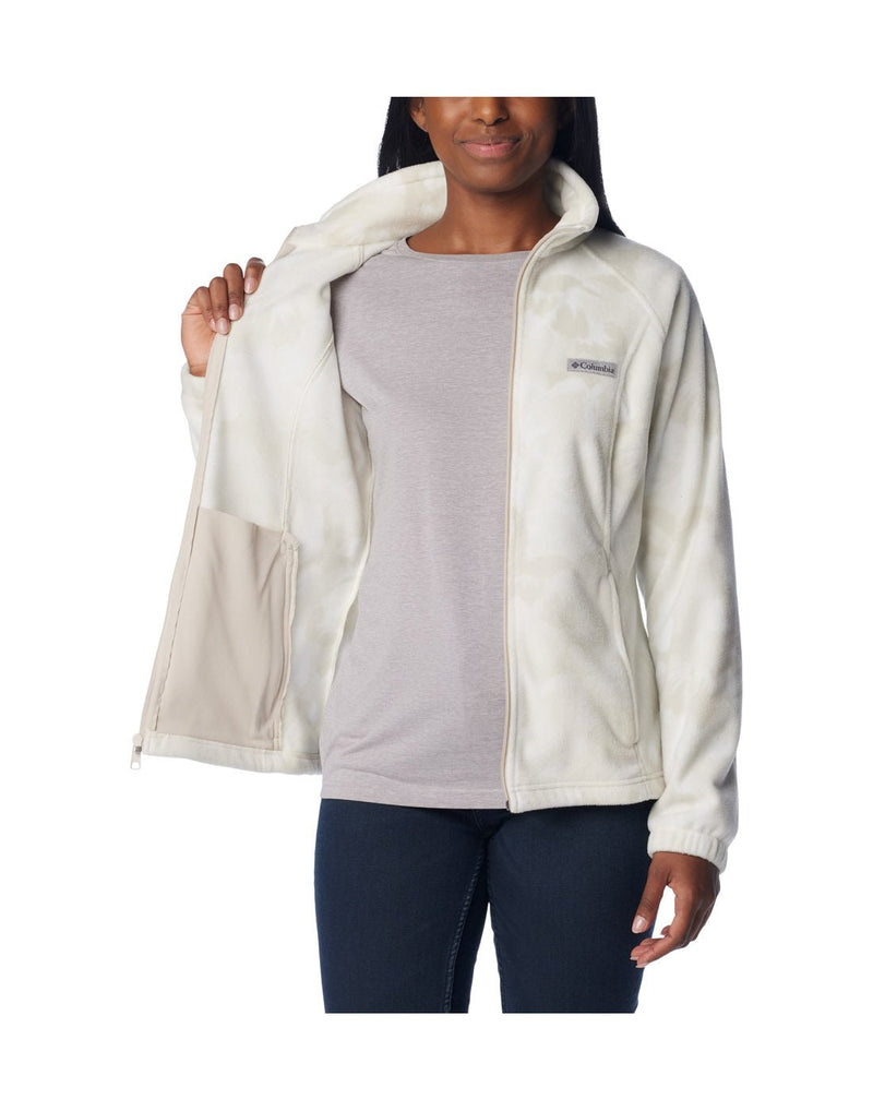 Woman wearing dark blue jeans and Columbia Women's Benton Springs™ Printed Full Zip Fleece Jacket in dark stone peonies, white with light beige floral pattern, front view, unzipped, with grey t-shirt beneath, holding one side open to show interior