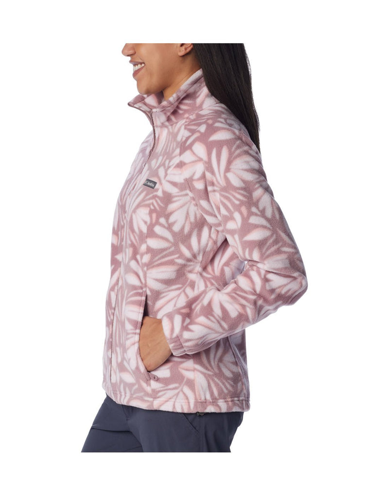 Woman wearing navy blue pants and Columbia Women's Benton Springs™ Printed Full Zip Fleece Jacket in fig areca, pink with white floral pattern, side view, zipped up with one hand in pocket