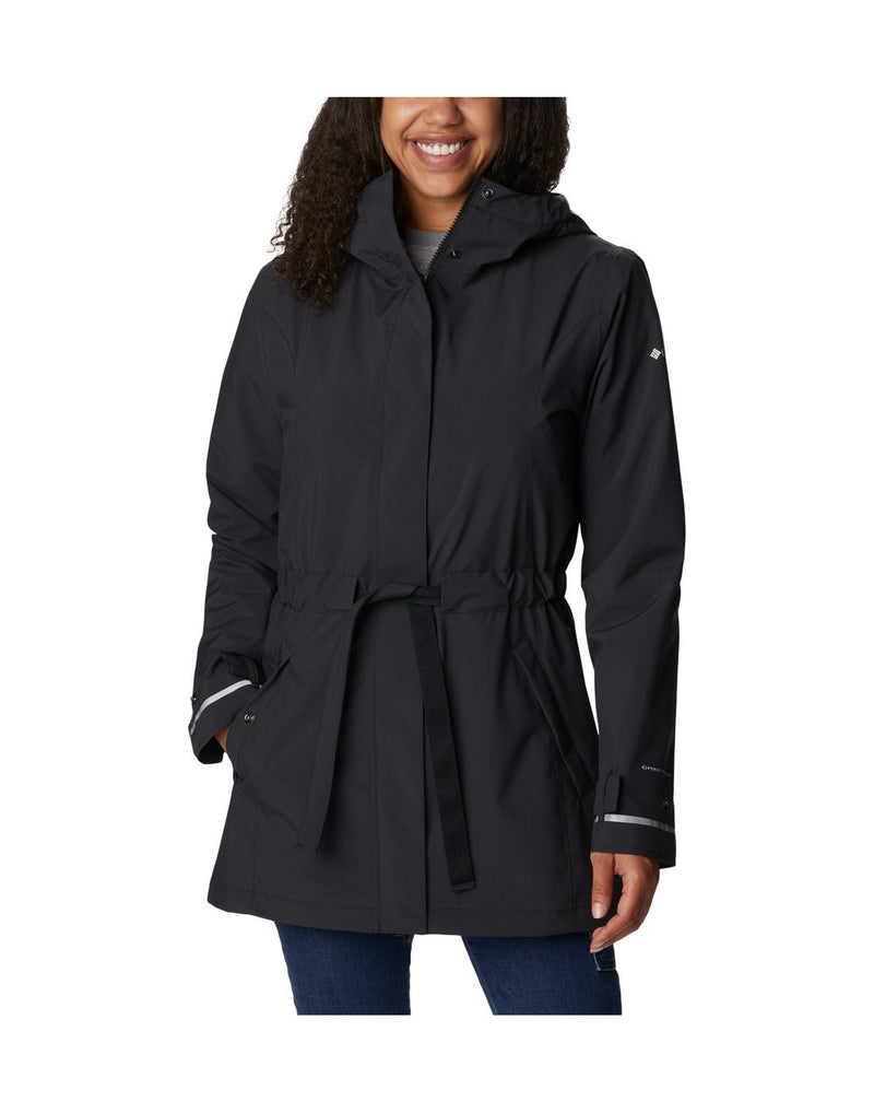 Woman wearing Columbia Women's Here and There™ II Rain Trench in black, front view, which reaches mid-thigh, zipped up and tied at waist