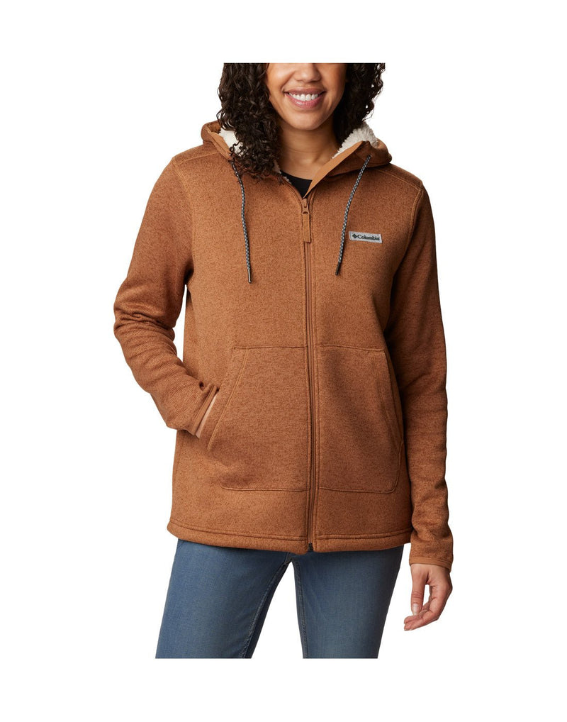 Front view of a woman wearing the Columbia Women's Sweater Weather™ Sherpa Full Zip Hooded Jacket in Camel Brown Heather colour, hood down, hand in right side pocket.