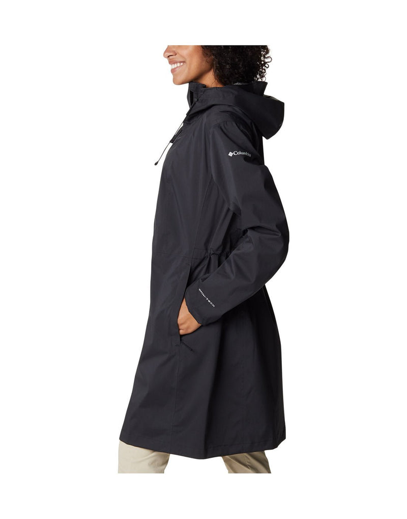 Woman wearing Columbia Women's Weekend Adventure™ Long Shell Jacket in black, zipped up, side view with hands in pockets