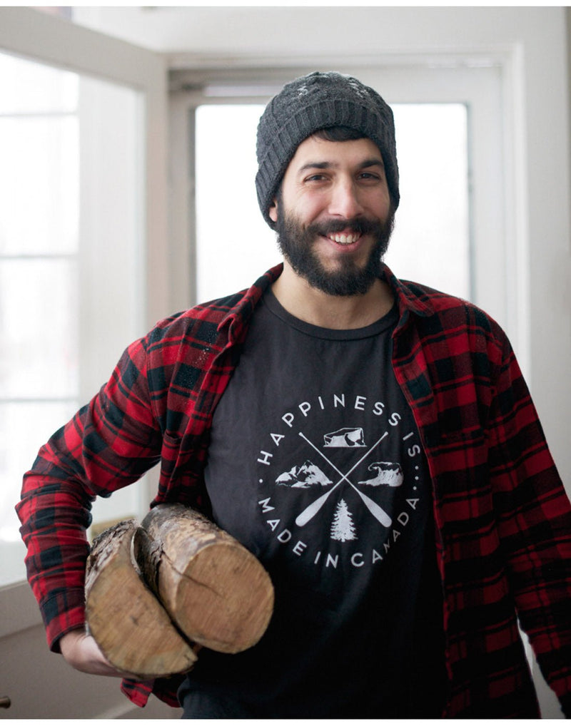 Bearded man holding two logs and wearing grey knit hat and Happiness Is... Men's Crest T-Shirt in vintage black with black and red check shirt open on top