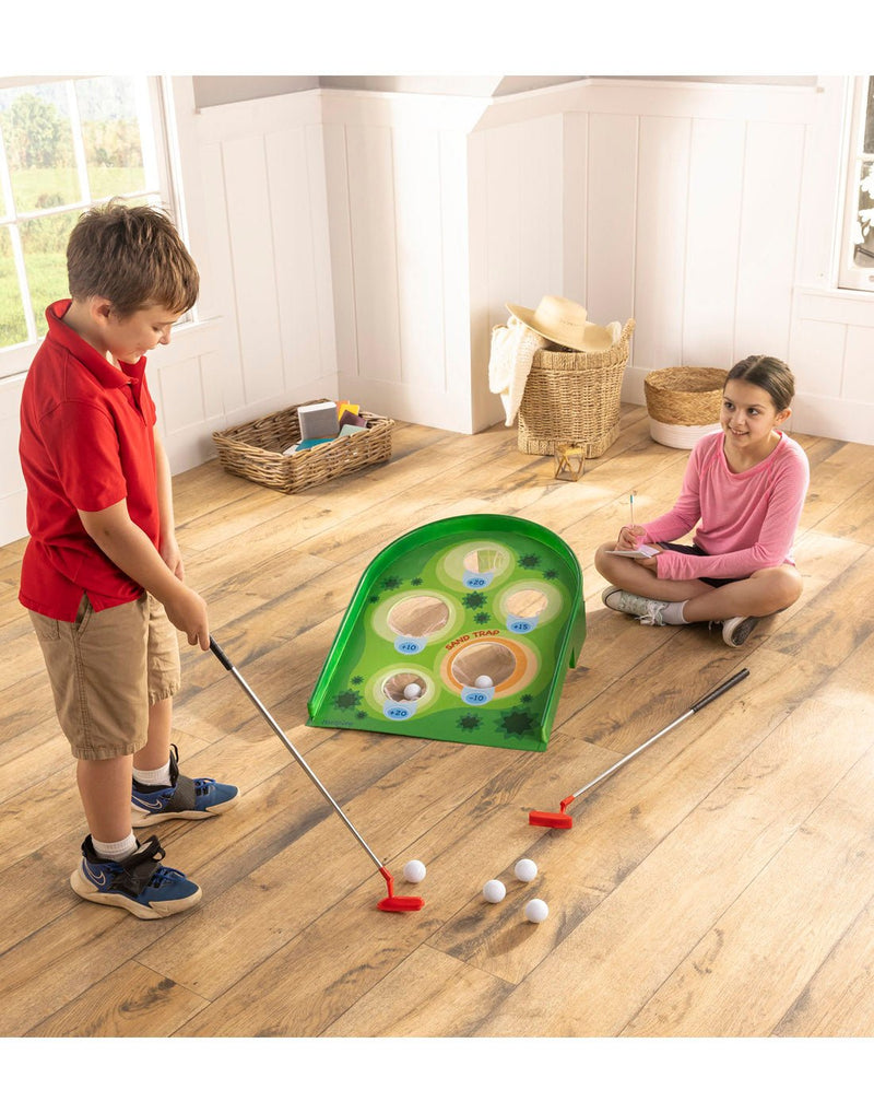 Two children playing the Arcade Golf Putting Game indoors, girl is sitting on a wood floor with score pad and pen and boy is lining up a shot