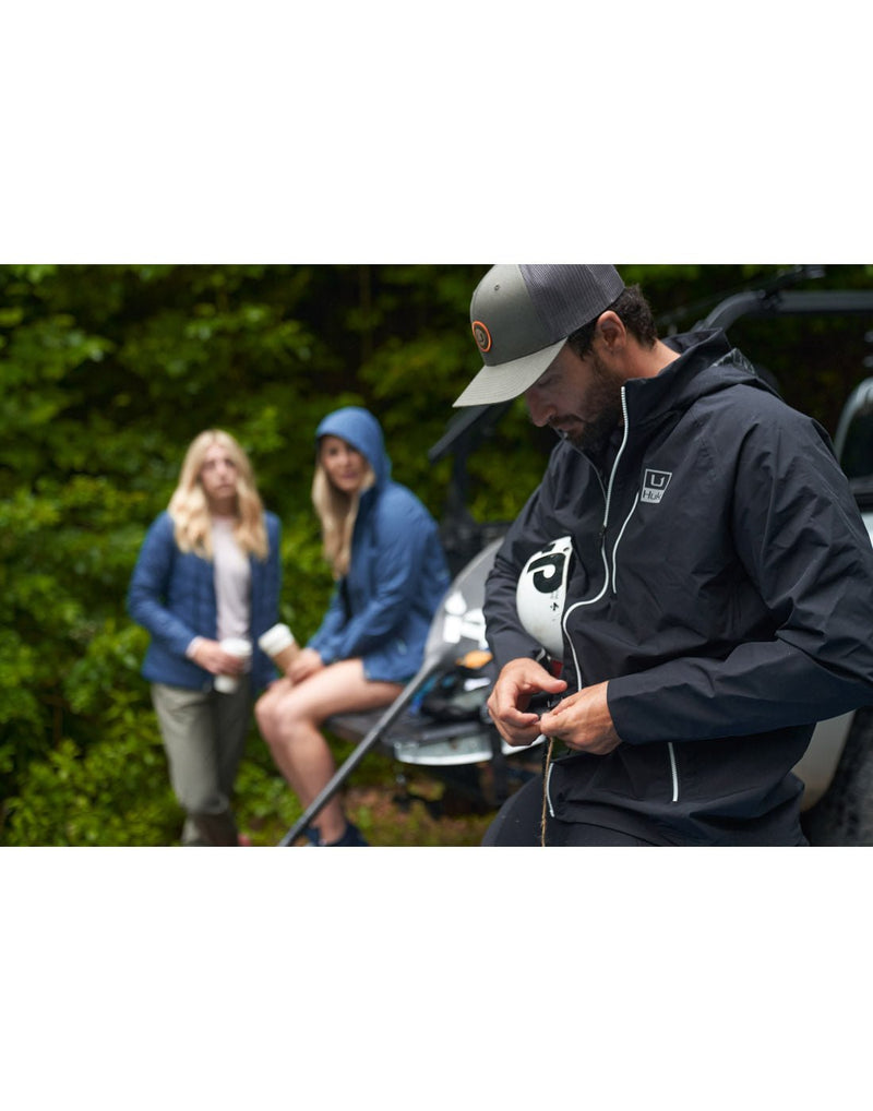 Lifestyle image of a man outdoors wearing the Huk Men's Pursuit Jacket in black.