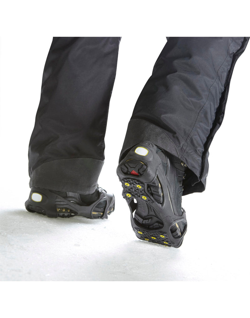 Person wearing snowpants and Icetrax IT11 Pro Tungsten Grip Ice Cleats on winter boots walking on snow