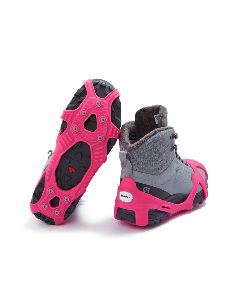 Icetrax V3 Tungsten Ice Cleats in bright pink on a pair of grey hiking boots, back view, one boot is upturned to show bottom cleats