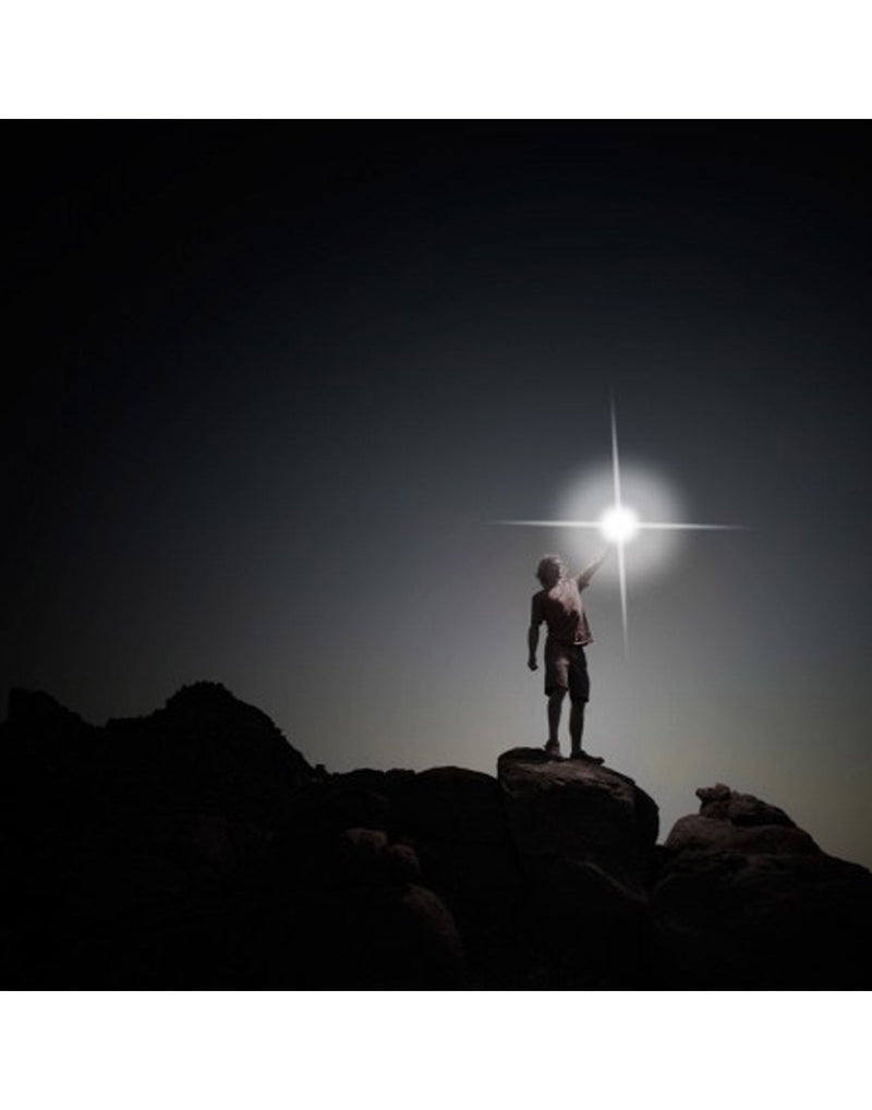 Man standing on a rock in the dark with beacon light on and shining into the night sky