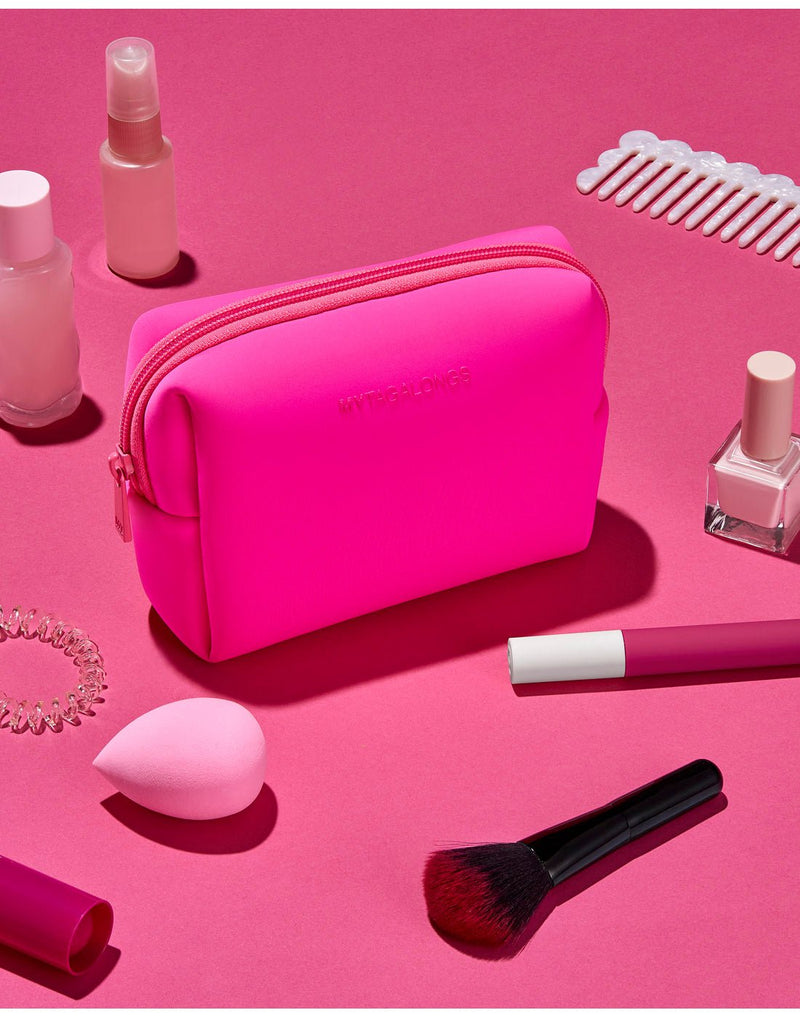Pink product spread - hot pink cosmetic case on a hot pink surface with make-up brush, sponge, comb, nail polish and other small bottles scattered around