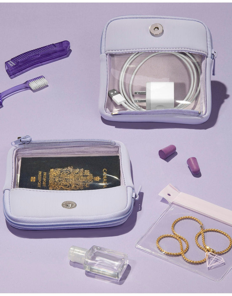 Purple product spread - lilac pouches detached and laid on a purple surface. There is a purple toothbrush and holder, purple ear plugs, a small clear bottle of sanitizer and a clear jewlery pouch with a gold necklace inside, all scattered about.  In one of the pouches is a Canadian passport and in the other is a white phone charger and cord.