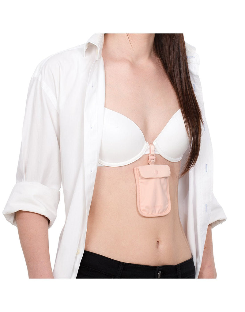 Woman with white shirt unbuttoned to show Pacsafe Coversafe® S25 Secret Travel Bra Pouch in orchid pink attached to center of white bra
