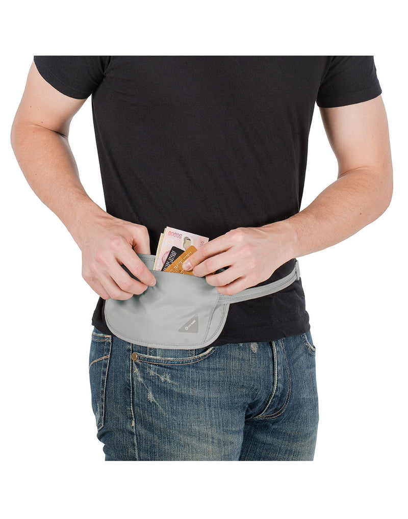 Man wearing jeans and a black t-shirt with the Pacsafe Coversafe® X100 RFID Blocking Security Waist Wallet in grey, reaching for some cash and credit cards inside