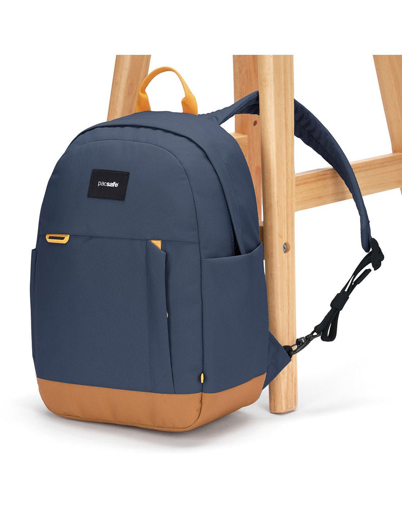 Pacsafe® Go 15L Anti-theft Backpack, coastal blue colour with tan bottom gusset, with one strap secured to chair leg.
