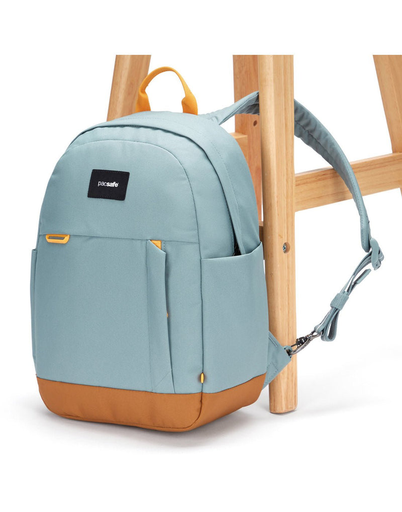 Pacsafe® Go 15L Anti-theft Backpack, fresh mint colour with tan bottom gusset, with one strap secured to chair leg.