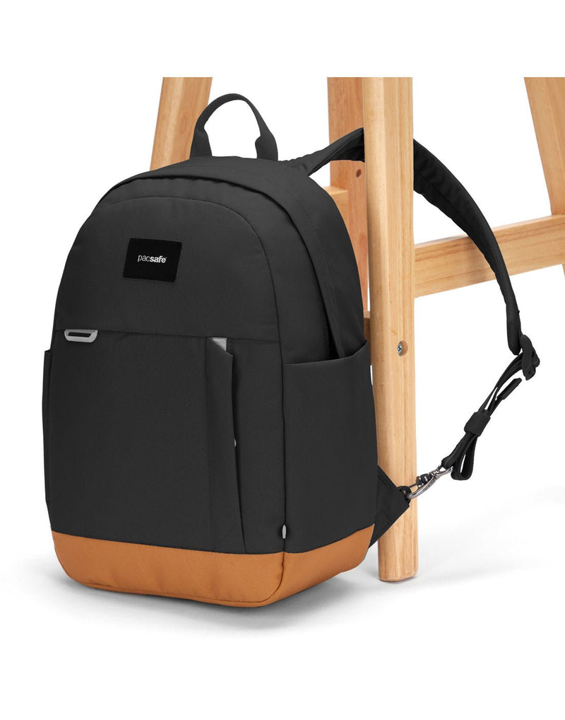 Pacsafe® Go 15L Anti-theft Backpack, jet black with tan bottom gusset with one strap secured to chair leg.