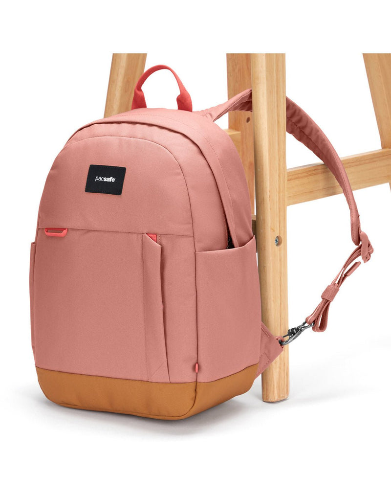 Pacsafe® Go 15L Anti-theft Backpack, rose colour with tan bottom gusset, with one strap secured to chair leg.