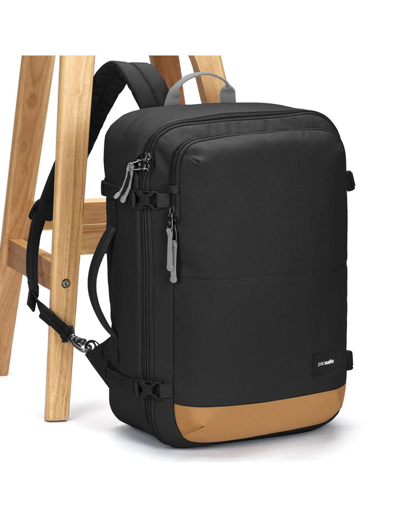 Pacsafe® Go 34L Anti-theft Carry-on Backpack, jet black with tan bottom gusset with one strap secured to chair leg.