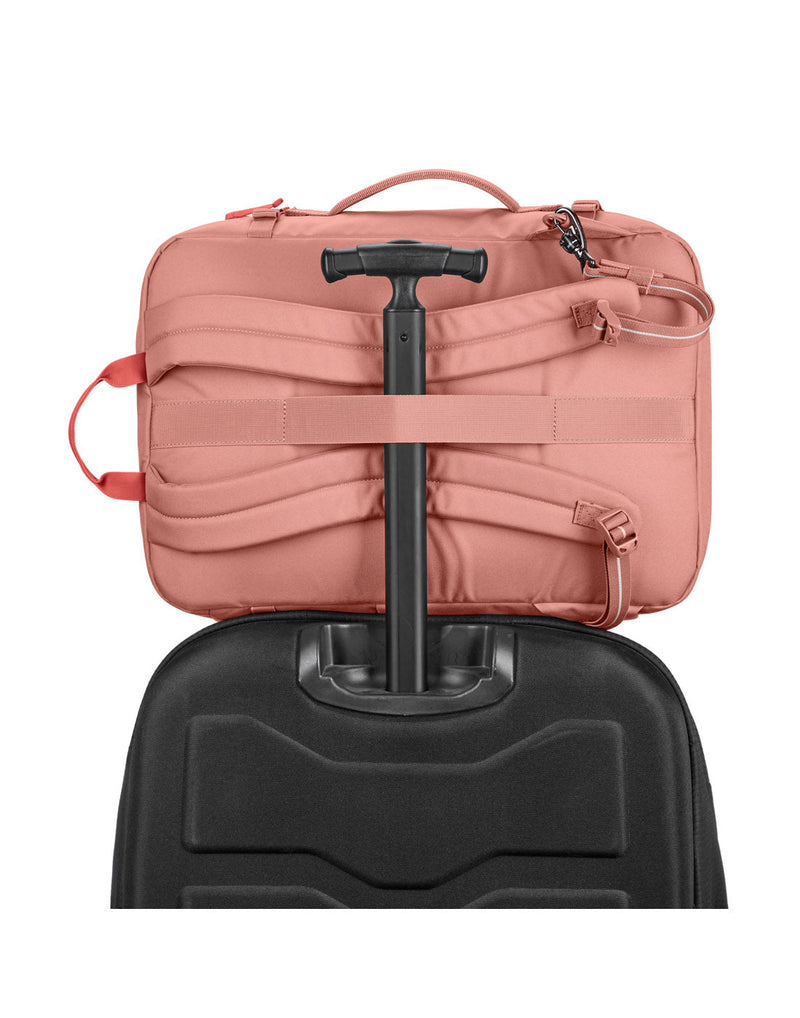 Pacsafe® Go 34L Anti-theft Carry-on Backpack in rose colour secured onto the extended handle of a full sized wheeled luggage.