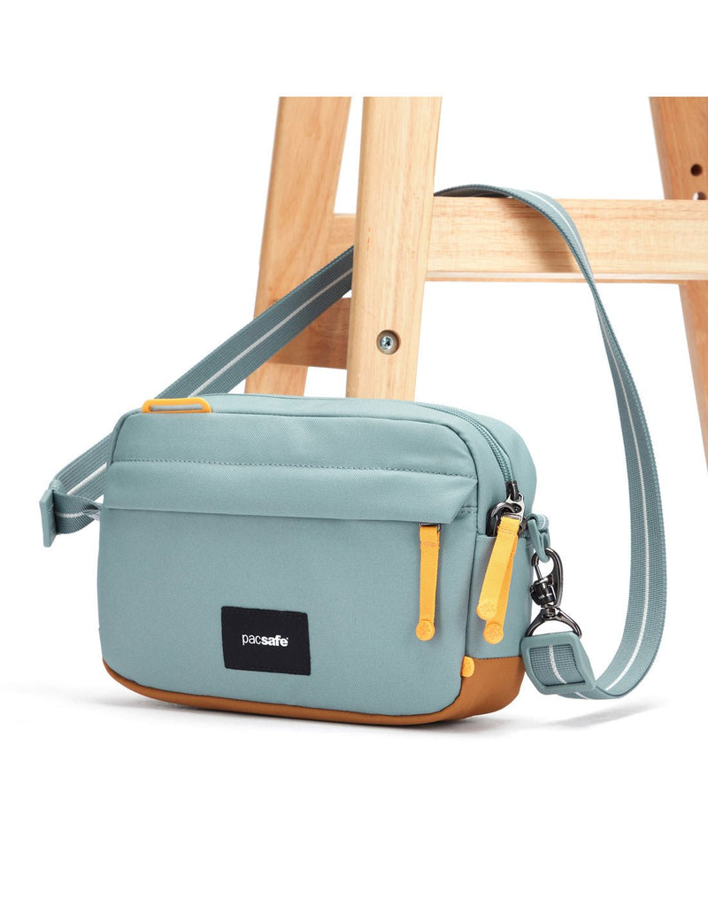 Pacsafe® GO Anti-Theft Crossbody Bag in fresh mint colour with shoulder strap secured to a chair leg.