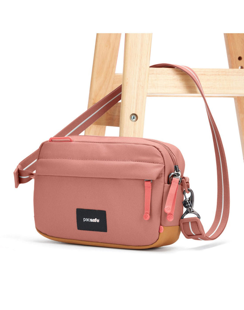 Pacsafe® GO Anti-Theft Crossbody Bag in rose colour with shoulder strap secured to a chair leg.
