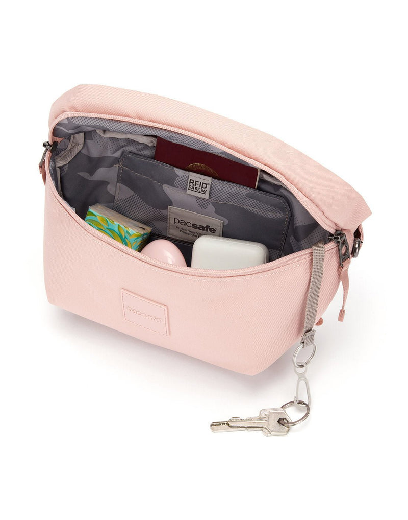 Pacsafe®Go Anti-Theft Sling Pack, sunset pink, unzipped to show interior with passport, tissues, ear pod case inside, and keys attached