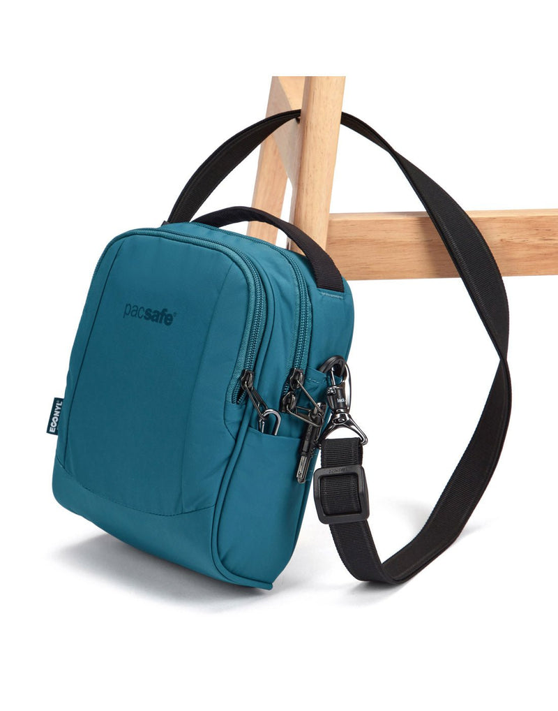 Pacsafe® LS100 Anti-theft Crossbody Bag, tidal teal, attached to chair leg with lockable shoulder strap