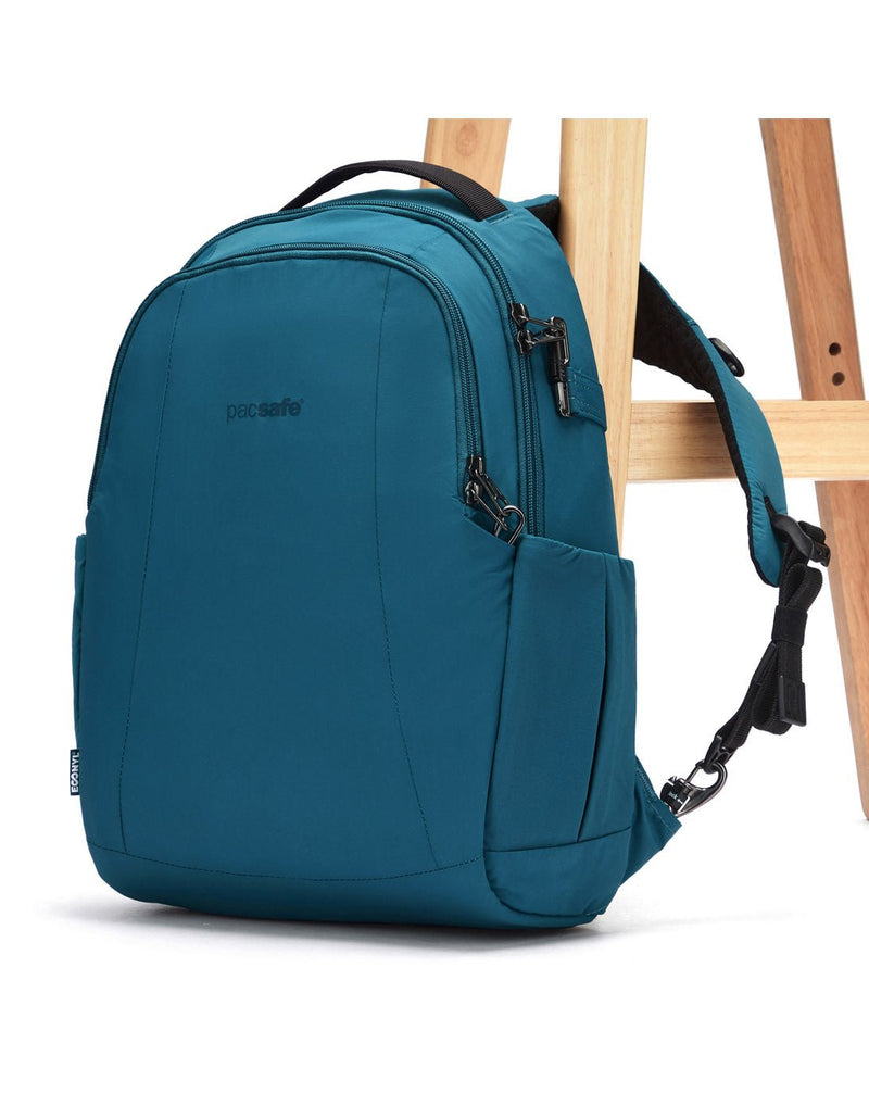 Pacsafe LS350 Anti-Theft 15L Backpack, tidal teal, attached to a chair leg with TurnNLock clip on one shoulder strap