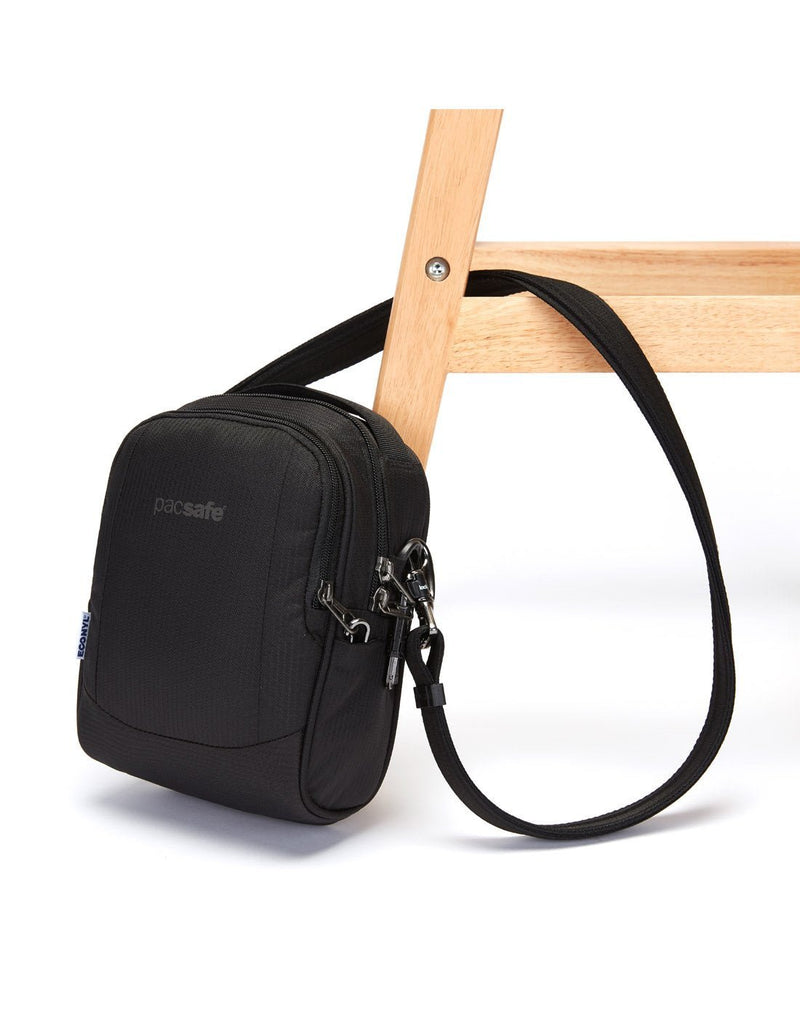 Pacsafe metrosafe ls100 econyl black colour recycled crossbody bag attached to a chair leg