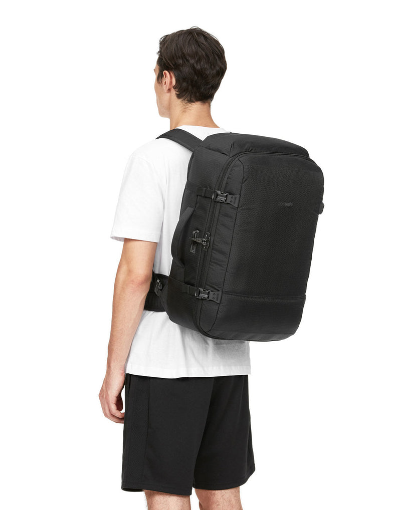 Man wearing white t-shirt and black shorts with the Pacsafe Vibe 40L Anti-theft Carry-on Backpack, black, on his back