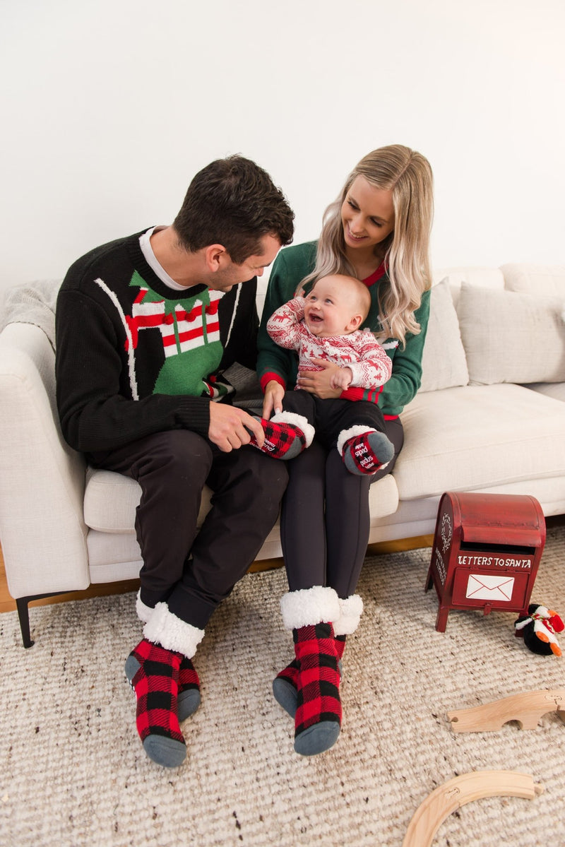 Man, woman and baby sitting on a couch wearing Christmas sweaters and Pudus Classic Slipper Socks in Lumberjack Red
