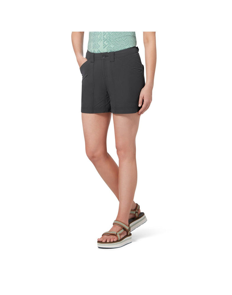 Bottom half of woman wearing turquoise shirt tucked into Royal Robbins Women's Backcountry Pro Shorts in charcoal.  One hand is in right pocket and woman is wearing sandals.