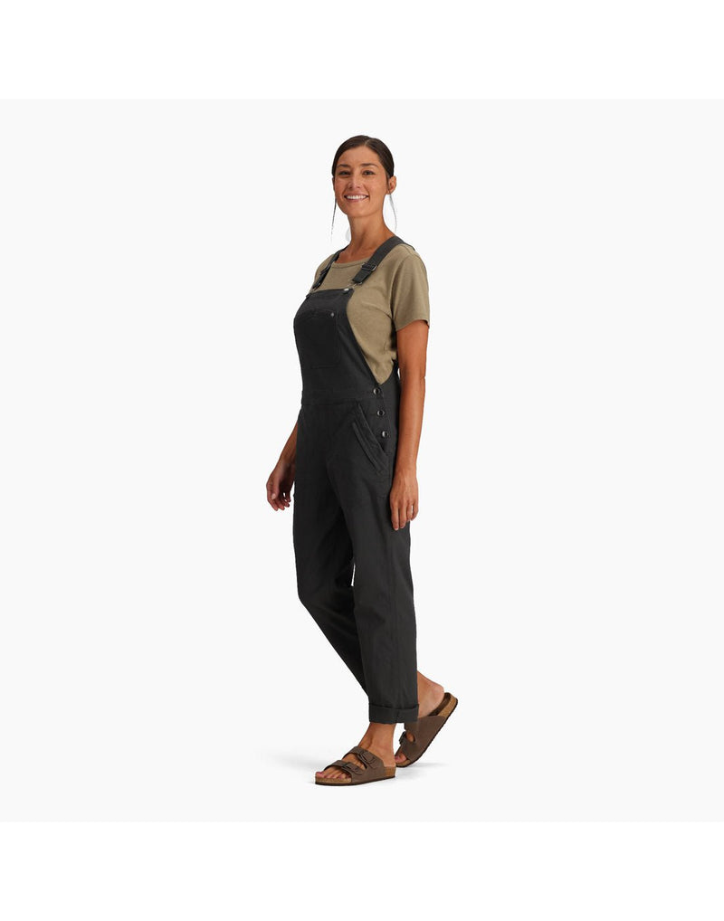 Woman wearing Royal Robbins Women's Half Dome Overall in charcoal grey over a khaki t-shirt. Bottom of pants are rolled up and she is wearing sandals, side view