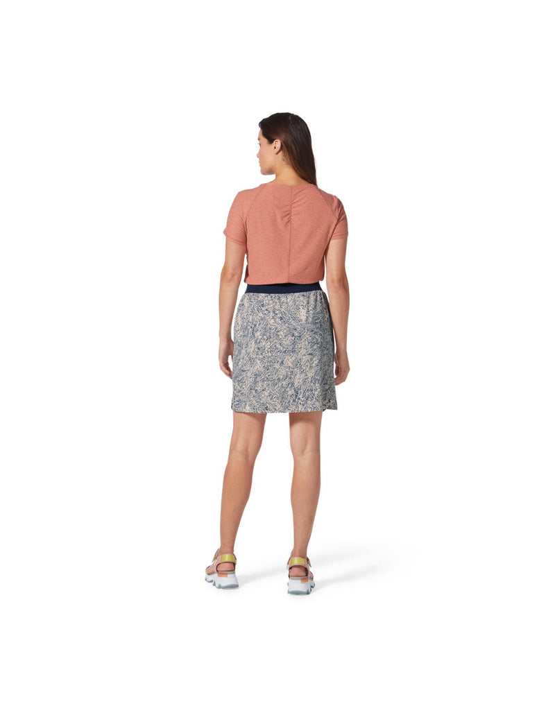 Back view image of a woman wearing Royal Robbins Women's Spotless Evolution Skirt in Powder Elkhorn Print, and a salmon colour short sleeve top.