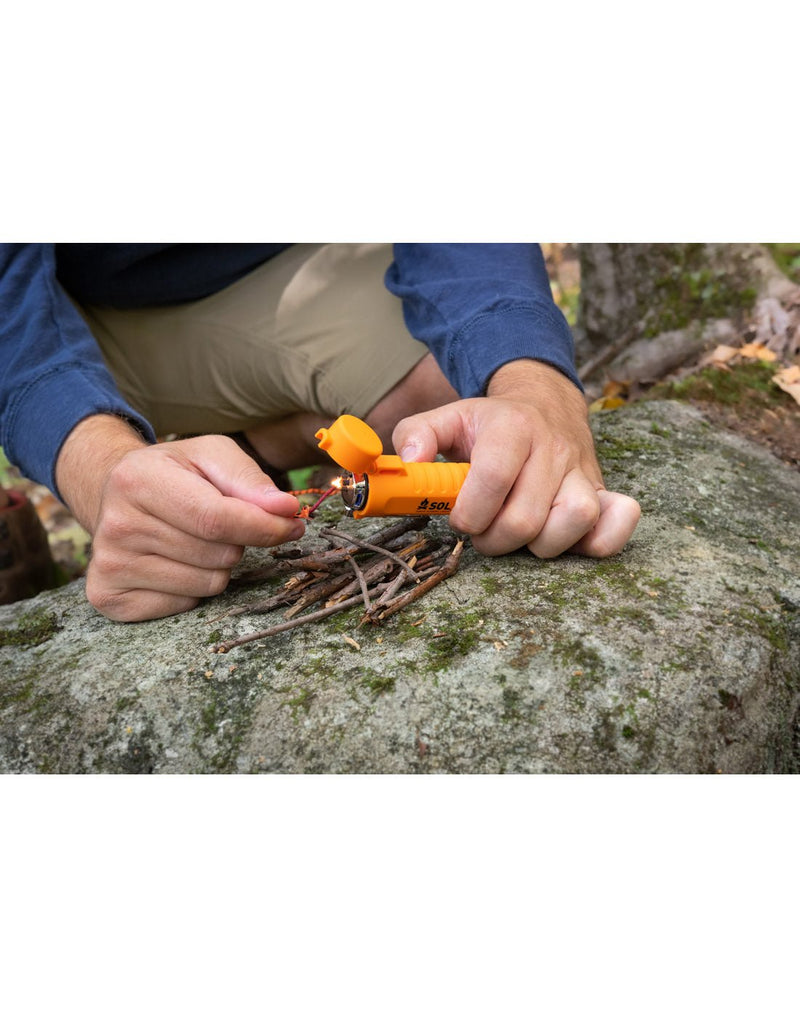 Person kneeling on a rock lighting some twigs with the SOL Fire Lite™ Fuel-Free Lighter