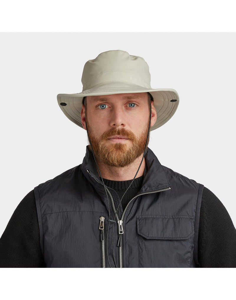Man wearing black sweater and vest and Tilley Rain Hat in stone, front view