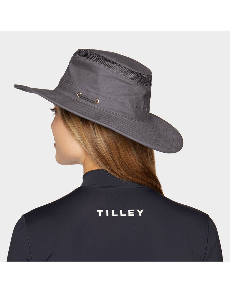 Portrait image of a woman wearing black zip up shirt and Tilley T4MO-1 Hiker's Hat in grey, back angled view