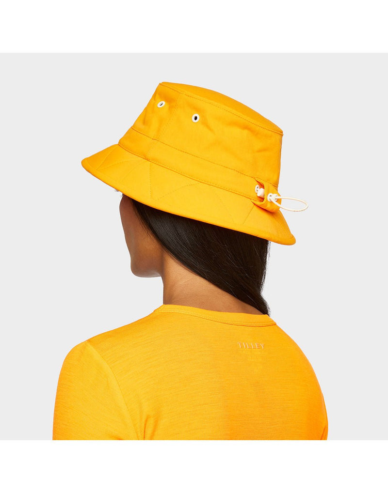 Portrait image of woman wearing Tilley Tofino Bucket Hat in bright orange with matching shirt, back angled view