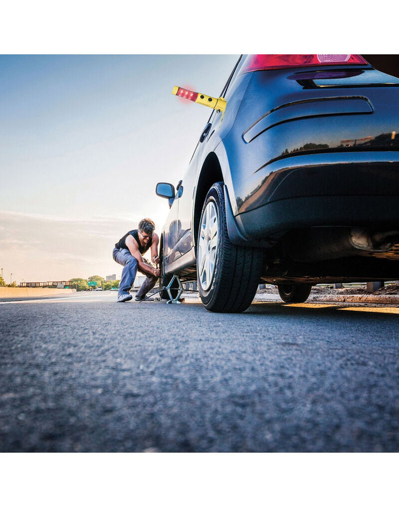 Lifestyle image of a man changing a car tire with the Travelon 4-in-1 Emergency Car Tool magnet attached to side of car